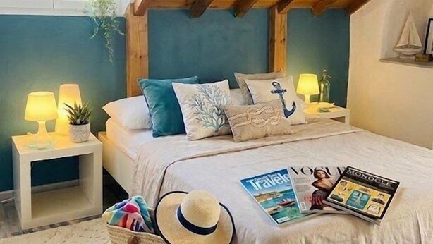 Een gezellig slaapkamer met een schuine kap, een bed met marineblauwe kussens, nachtlampjes, een kleine plant en een reisblad op het bed.