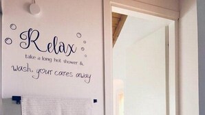 Een badkamer met een handdoek aan een rek, een bordje met de tekst 'Relax' en een melding over een lange, warme douche.