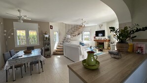 Een ruime woonkamer met een eettafel, een trap, een open haard en een aan de muur bevestigde televisie.