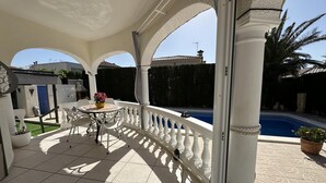 Een overdekt buitengebied met een zwembad, witte zuilen en een tafel met stoelen.