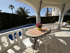 A covered outdoor area with a pool, white chairs, and a table with a vase of flowers. - Honduras beautiful house with private pool in Miami-Platja! (Mont-roig del Camp)