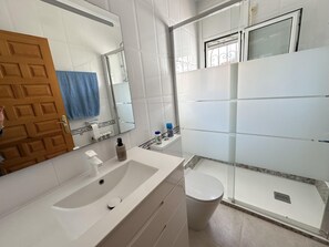 A bathroom with a white sink, mirror, toilet, and shower area. - Honduras beautiful house with private pool in Miami-Platja! (Mont-roig del Camp)
