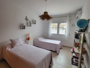 A bedroom with two beds, a bedside table with a lamp, a hanging light fixture, a window with a view, and a bookshelf with books and a globe. - Honduras beautiful house with private pool in Miami-Platja! (Mont-roig del Camp)