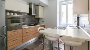 Una cucina moderna con forno integrato, elettrodomestici in acciaio inossidabile e un'area pranzo bianca con sgabelli da bar.
