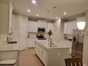 Una cucina moderna con mobili bianchi, elettrodomestici in acciaio inossidabile e illuminazione a sospensione.