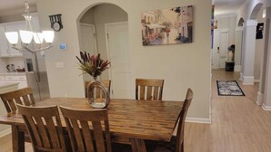 A dining area with a wooden table and chairs, a vase with flowers, a chandelier, and a painting on the wall.