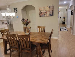 A dining area with a wooden table and chairs, a vase with flowers, a chandelier, and a painting on the wall.