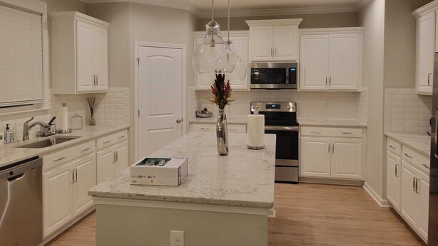 A modern kitchen with white cabinetry, a central island, stainless steel appliances, and a hanging light fixture.