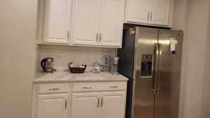 A kitchen with white cabinets, a stainless steel refrigerator, and a marble countertop.