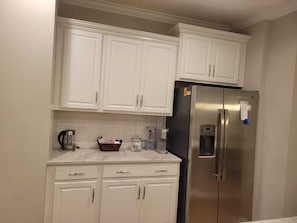 A kitchen with white cabinets, a stainless steel refrigerator, and a marble countertop.