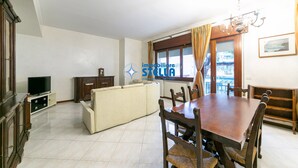 A living room with a sofa, TV, wooden dining table, chairs, and a chandelier. - Minetto / city center apt *Via Bafile* (Jesolo)