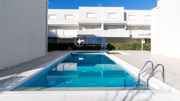Una piscina con agua azul cristalina, rodeada por un edificio blanco con balcones y un cartel que dice 'Immobiliare STELLA'.