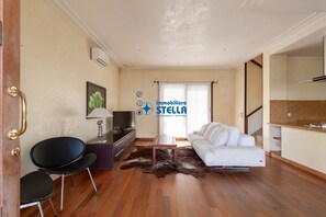 A modern living room with a sofa, chairs, a TV, and a dining area.