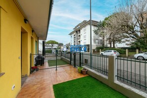 Un edificio amarillo con un patio amurallado, un pequeño jardín y una calle con coches estacionados.