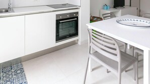 Una cucina moderna con mobili bianchi, forno integrato, lavello e zona pranzo con tavolo e sedie bianche.