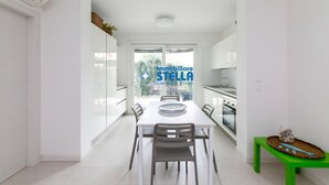 Una cucina moderna con mobili bianchi, un tavolo da pranzo con sedie e una panca verde con un cesto.