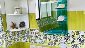 A bathroom with a white sink, green and white patterned tiles, a mirror, and a shelf with decorative items.