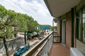 Un balcon donnant sur une rue, des arbres et un immeuble avec une enseigne.
