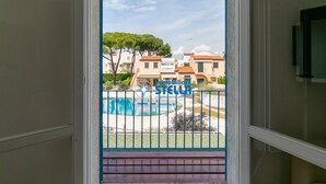 Blick von einem Balkon mit Pool, blauem Zaun und Gebäuden im Hintergrund.