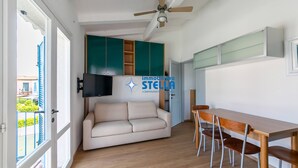 Ein Wohnzimmer mit einer Couch, einem Esstisch mit Stühlen, einem Deckenventilator und einem an der Wand montierten Fernseher.