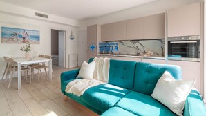 Una sala de estar moderna con un sofá color turquesa, una mesa de comedor con sillas y una zona de cocina con armarios y un horno.