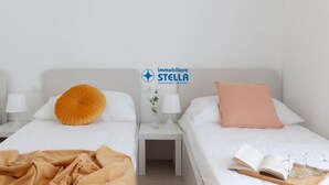 Habitación de hotel con dos camas, una mesita de noche con lámpara, un florero con flores y un cartel con el nombre del hotel.