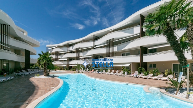 Un hotel moderno con piscina, sillas de descanso y palmeras.