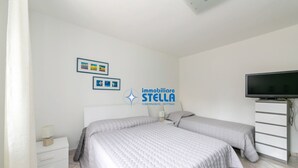 Ein Schlafzimmer mit zwei Betten, einem Fernseher, einem Nachttisch und einer Kommode.