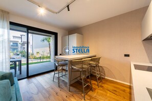 A modern kitchen with a dining area, a large window, and a logo for 'immobiliare STELLA'. - Caribe Sunset #pool# / °parking° (Lido di Jesolo)