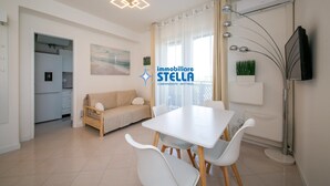 Un soggiorno moderno con angolo pranzo, divano, televisore e cucina sullo sfondo.