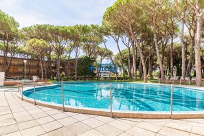 Ein von Bäumen umgebener Pool, im Hintergrund ein Gebäude.