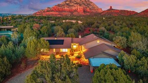 Una casa moderna con paneles solares, rodeada de árboles y una montaña al fondo.