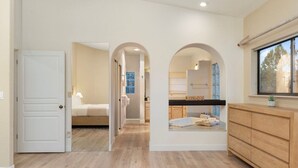 Un pasillo que da a un dormitorio, un baño y una zona de cocina con un armario de madera y una ventana.