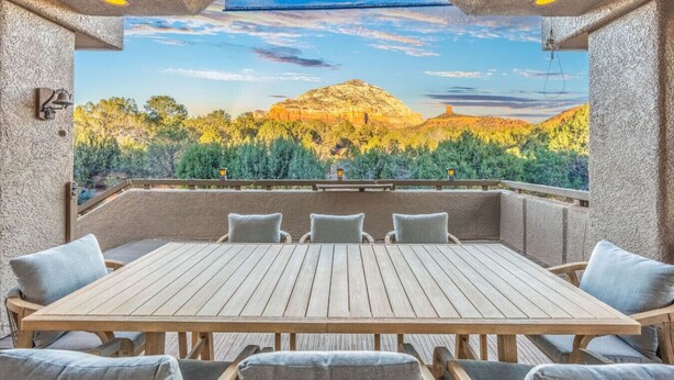 Un patio al aire libre con mesa y sillas de madera, vista a un paisaje montañoso y un muro de piedra.