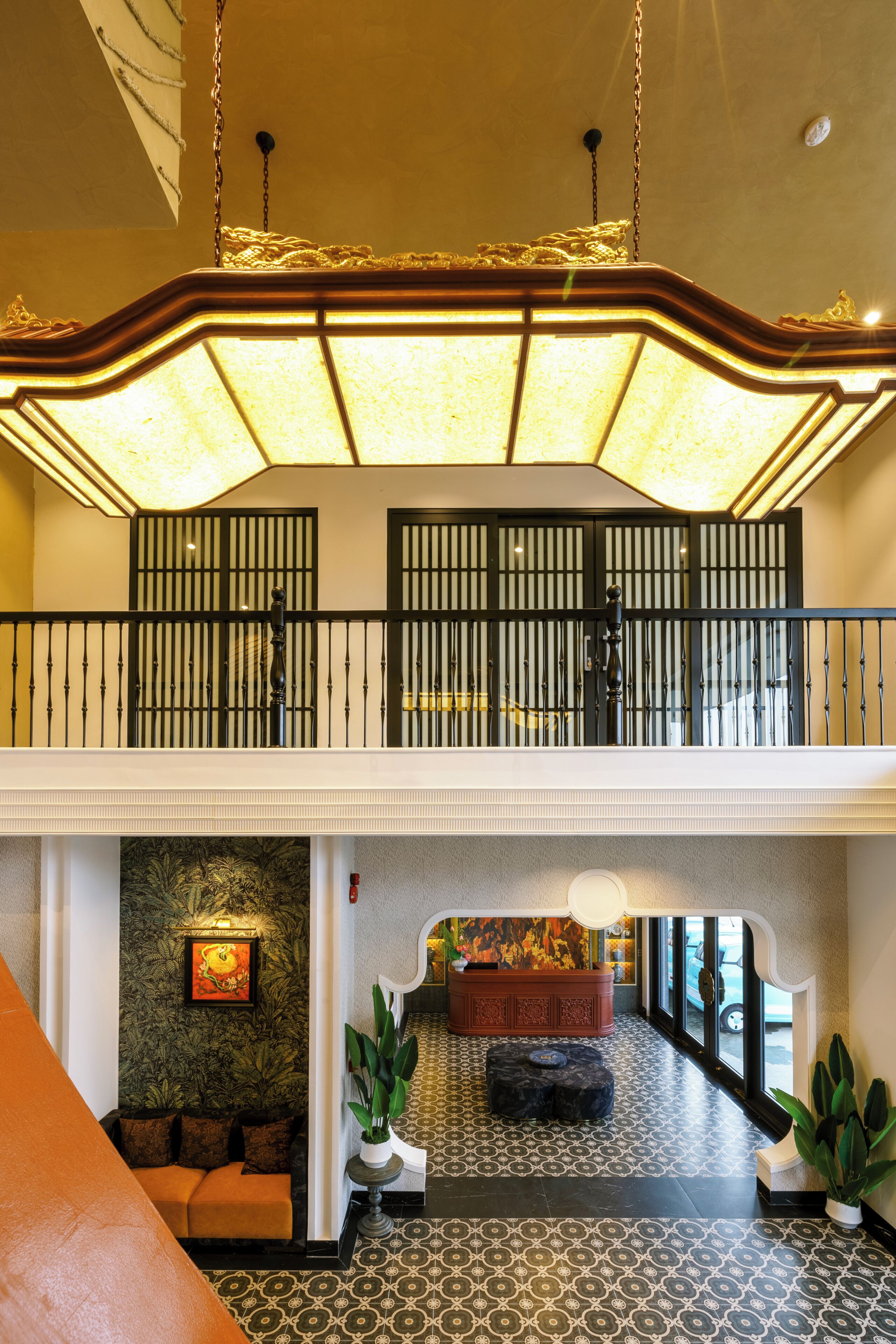 Um saguão de hotel com piso estampado, um sofá, uma planta e um lustre decorativo.