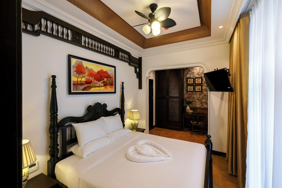 Une chambre d’hôtel avec un lit, un ventilateur de plafond, un tableau, une télévision et une vue sur l’extérieur.
