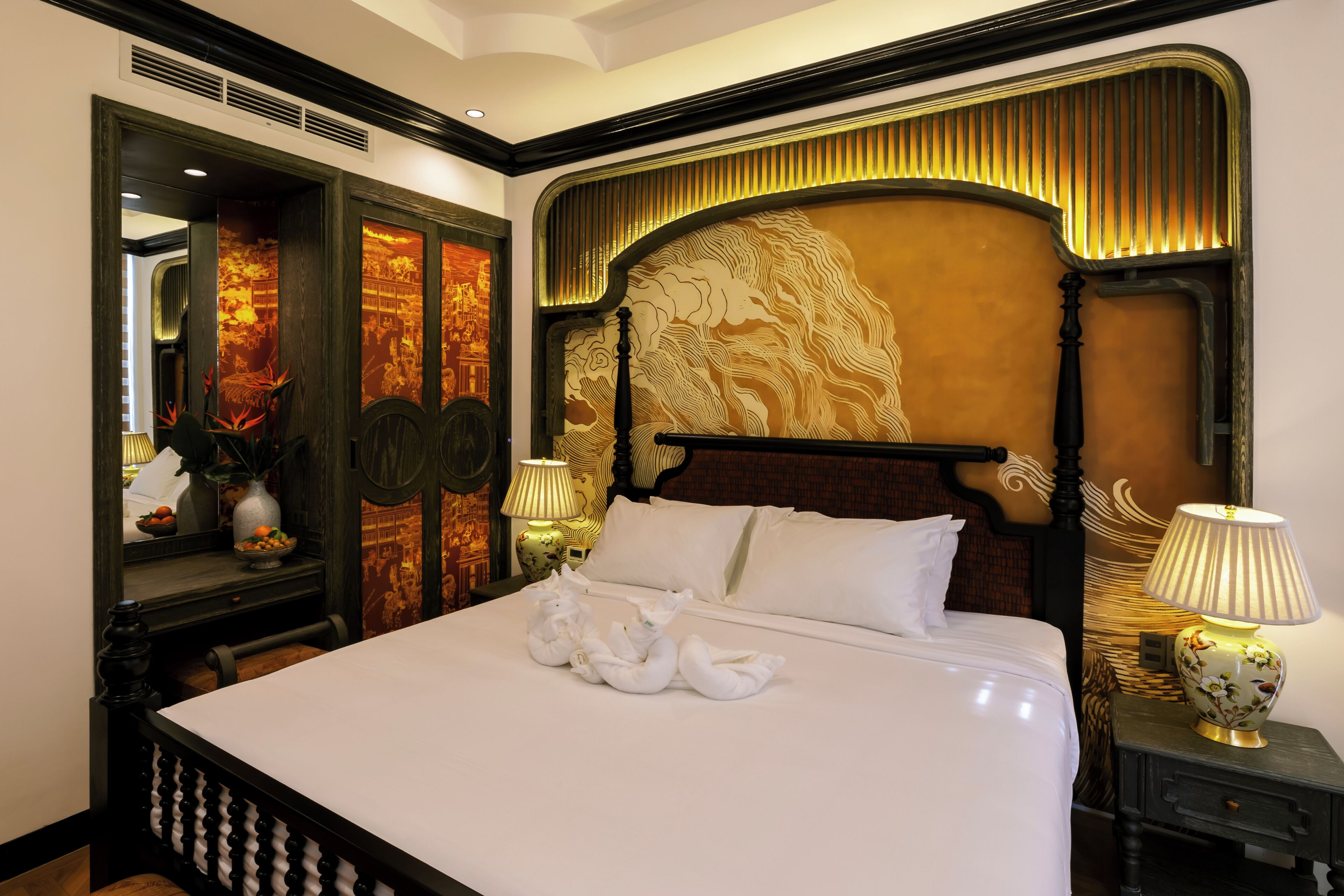 Una camera d'albergo con un letto grande, una testiera decorata, un comodino con una lampada e uno specchio.