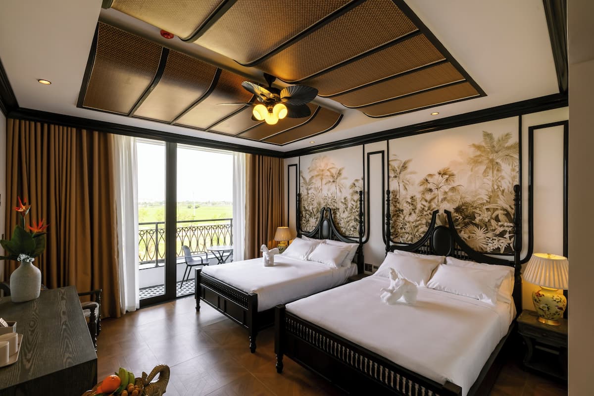 Une chambre d’hôtel avec deux lits, un coin repas, un balcon avec vue et un ventilateur de plafond.