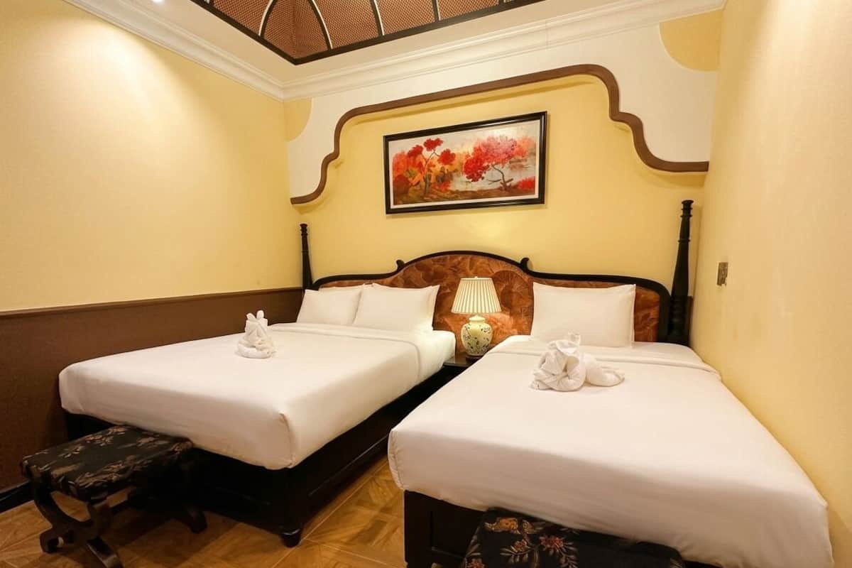 Une chambre d’hôtel avec deux lits, une tête de lit en bois, un tableau au mur et un banc.