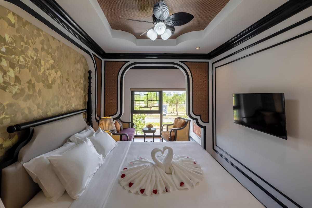 Une chambre d’hôtel équipée d’un lit, d’une télévision, d’un ventilateur de plafond et offrant une vue sur l’extérieur.