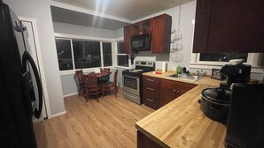 A kitchen with wooden cabinets, a stove, a microwave, and a dining area with chairs. - Convenient 2-bedroom House in downtown Bremerton Perfect for your Getaway (Bremerton)
