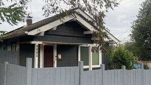 A house with a dark exterior, a white door, and a small porch with a picket fence. - Convenient 2-bedroom House in downtown Bremerton Perfect for your Getaway (Bremerton)