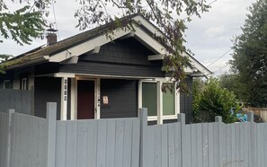 A house with a dark exterior, a white door, and a small porch with a picket fence. - Convenient 2-bedroom House in downtown Bremerton Perfect for your Getaway (Bremerton)