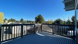 A wooden deck with a metal railing, overlooking a residential area with houses and trees. - Convenient 2-bedroom House in downtown Bremerton Perfect for your Getaway (Bremerton)