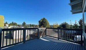 A wooden deck with a metal railing, overlooking a residential area with houses and trees. - Convenient 2-bedroom House in downtown Bremerton Perfect for your Getaway (Bremerton)
