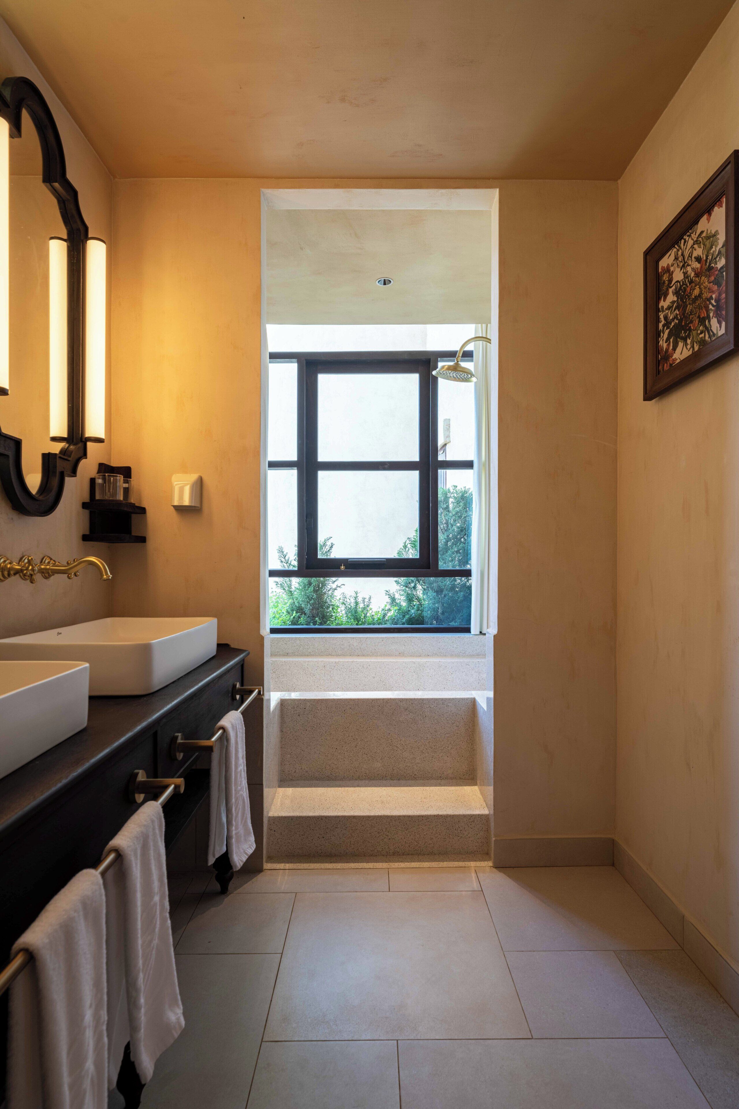 A bathroom with a large window, a bathtub, and a double sink with a mirror.