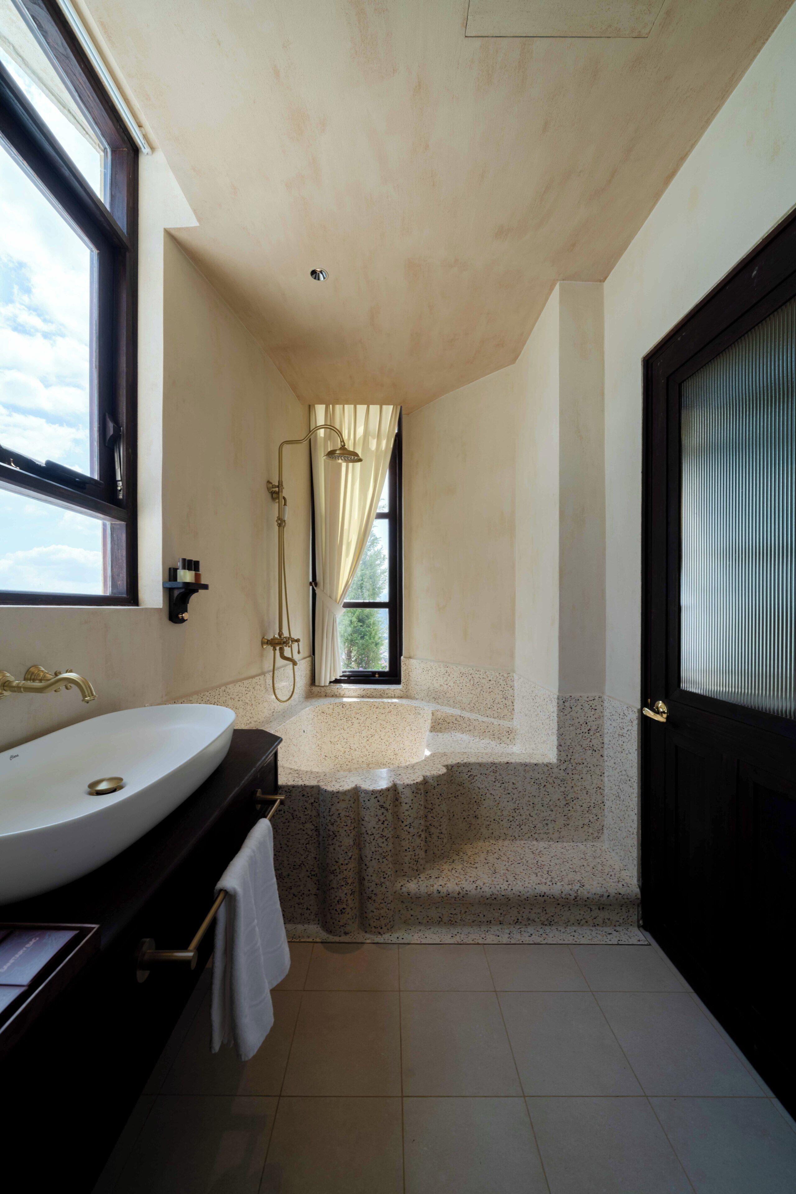 A bathroom with a large sink, a shower, and a door leading to a balcony.