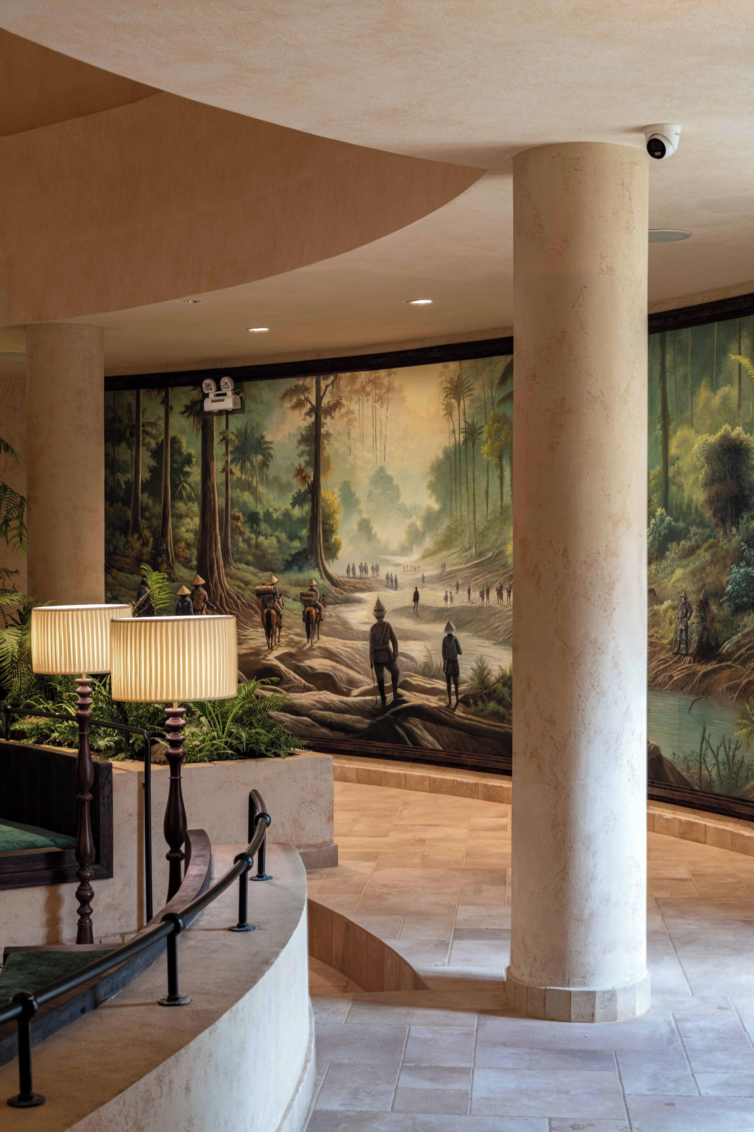 A lobby with a large mural, a curved staircase, and a security camera.