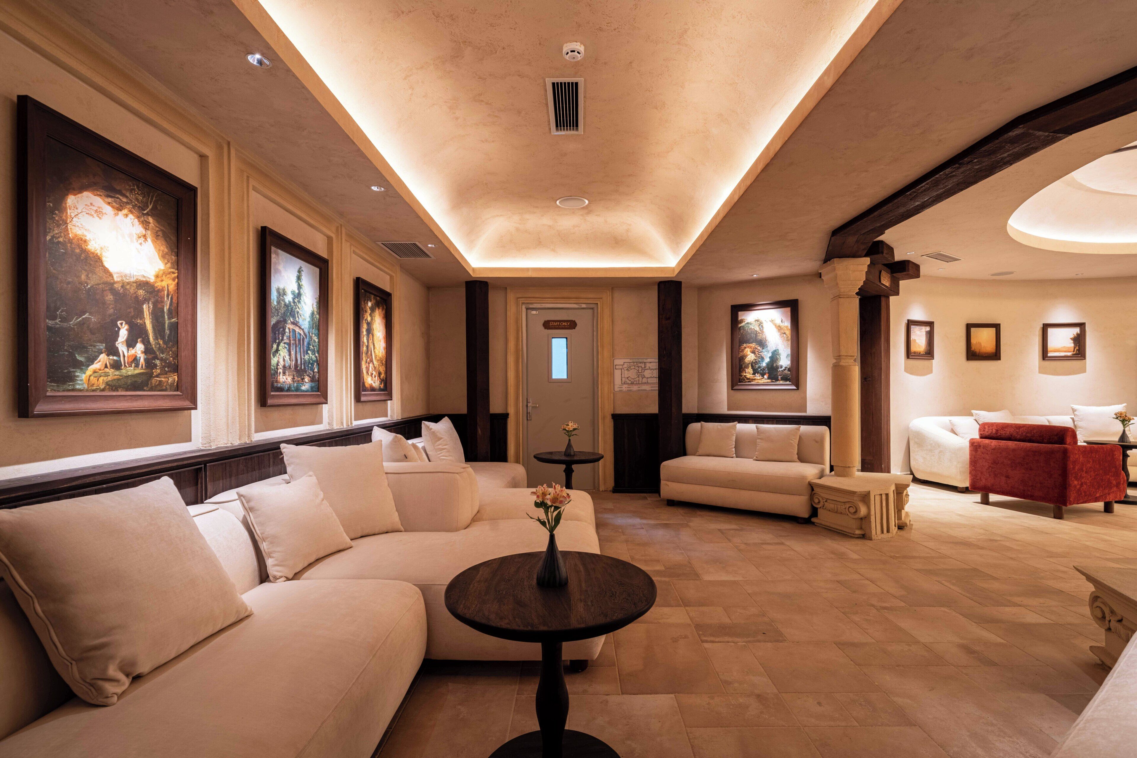 A spacious lobby with a beige sofa, a round table with a vase, and framed artwork on the walls.