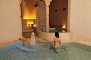 A woman sitting in a clear indoor pool with a warm light source in the background. - Hôtel Fantaisie (Da Lat)
